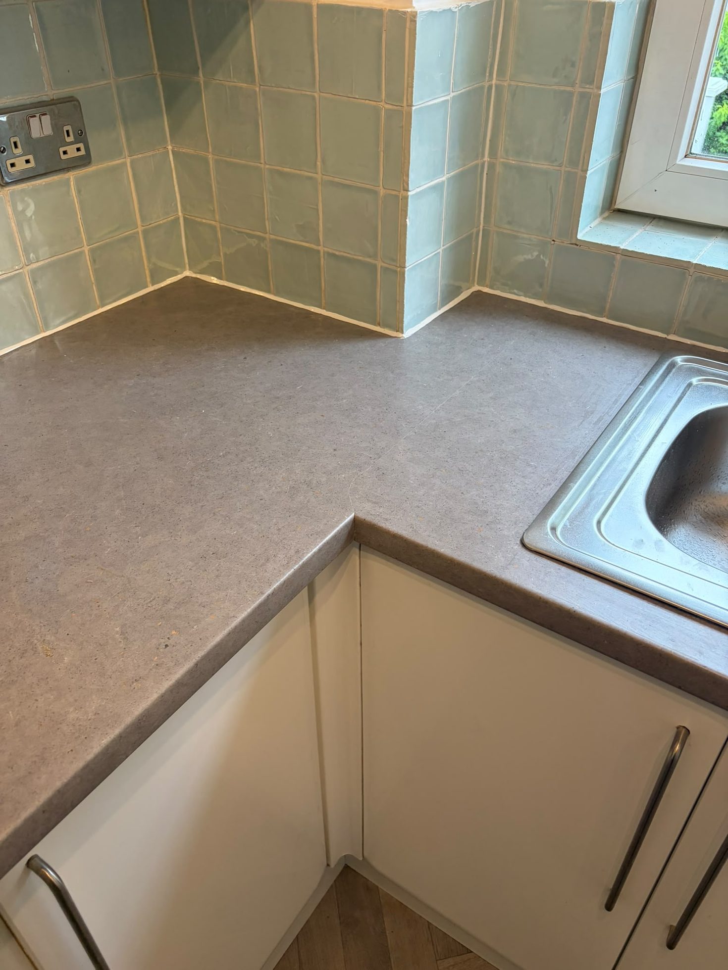 Fitted kitchen worktop scribed to a tiled splashback with an inset stainless sink