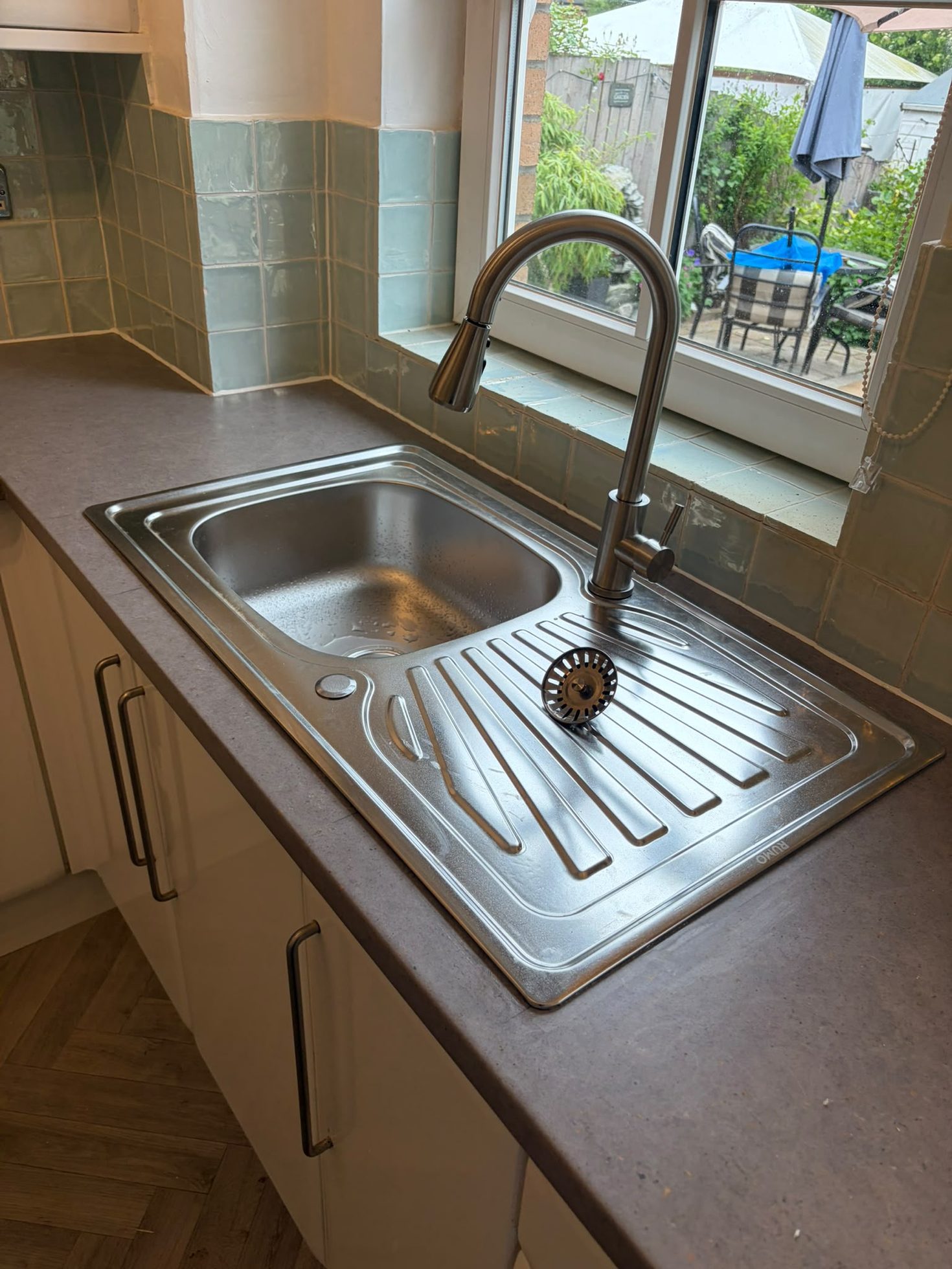 Stainless sink, drainer and tall chrome tap fitted beside white kitchen cabinetry